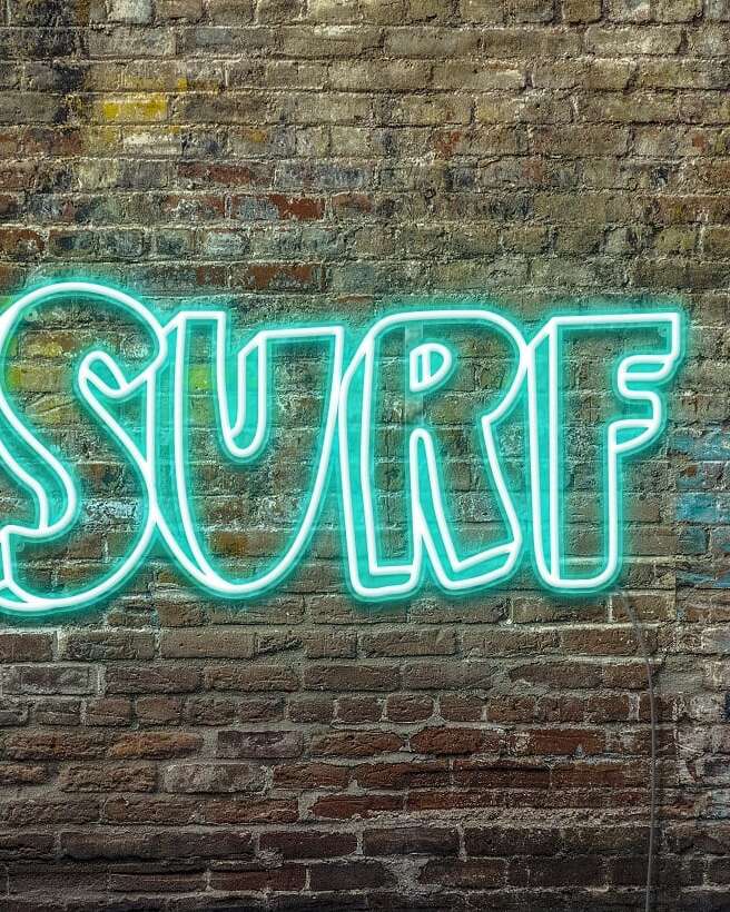 A personalized neon sign of the word 'surf' on a brick wall