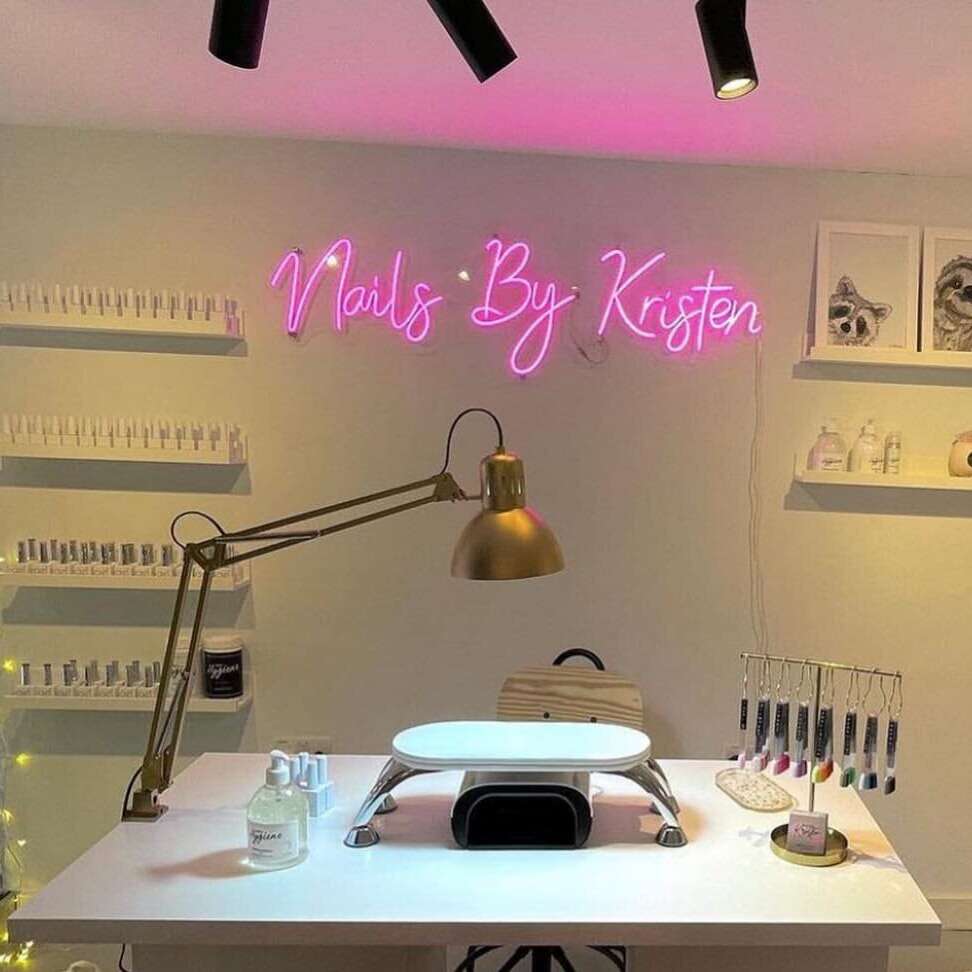 Neon salon name mounted on a wall behind a manicure table