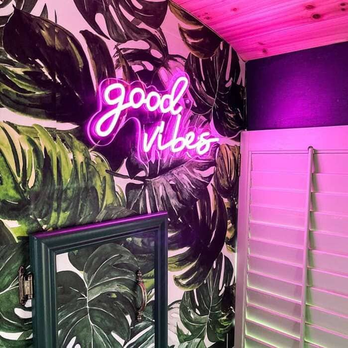 Pink Good Vibes bathroom neon sign with tropical leaf wallpaper