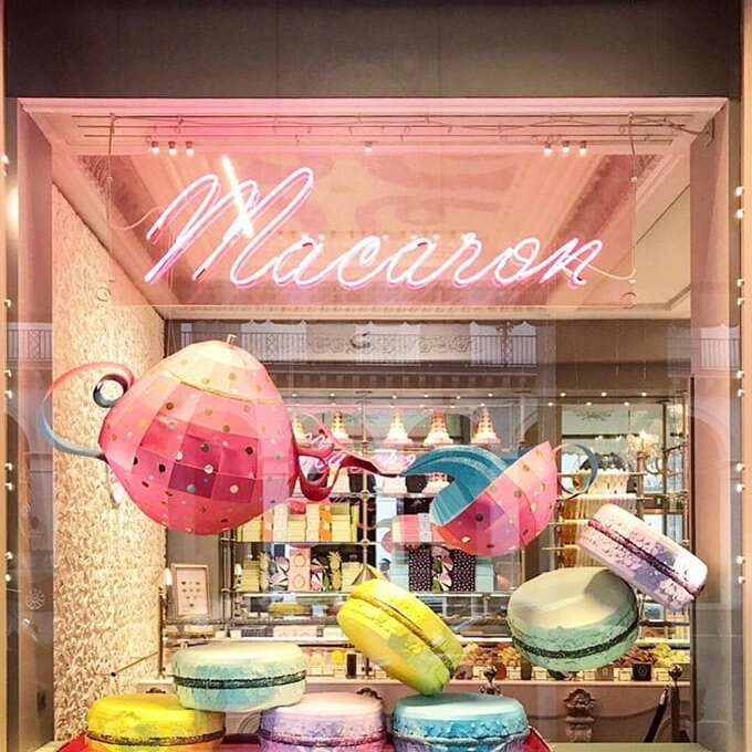 Pink Macaron glass neon sign above a colorful dessert shop window display