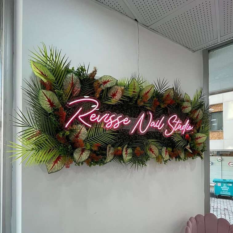 Pink neon lettering on a greenery wall in a nail salon