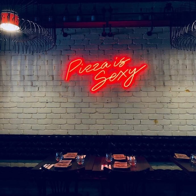 Red Pizza Is Sexy neon sign above a pizzeria dining booth