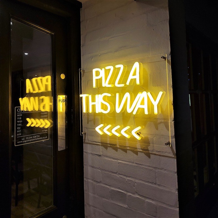 Yellow Pizza This Way custom neon sign with arrows at a pizza shop entrance